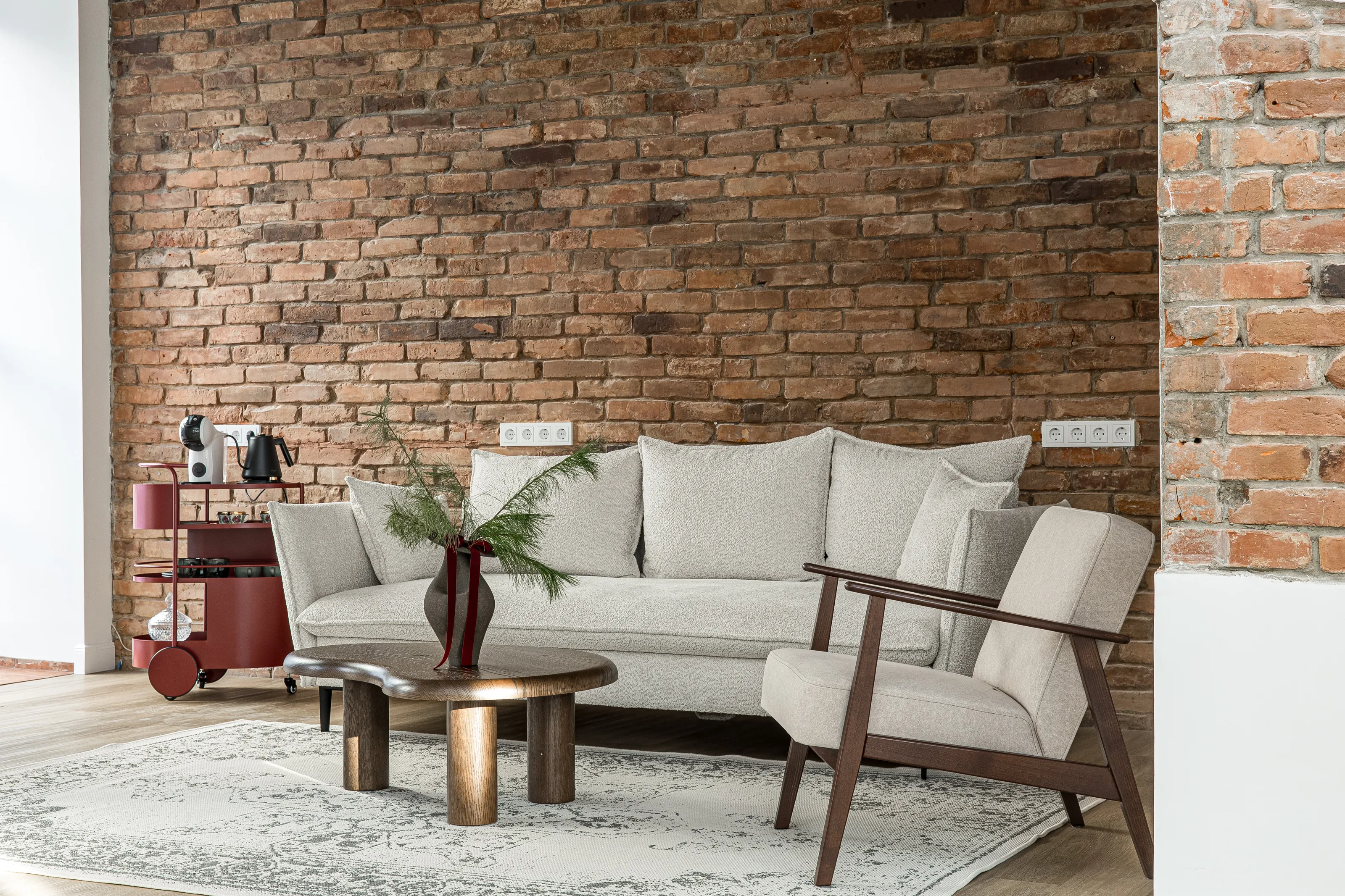 Sofa ir fotelis prie plytų sienos su mediniu staliuku ir vaza