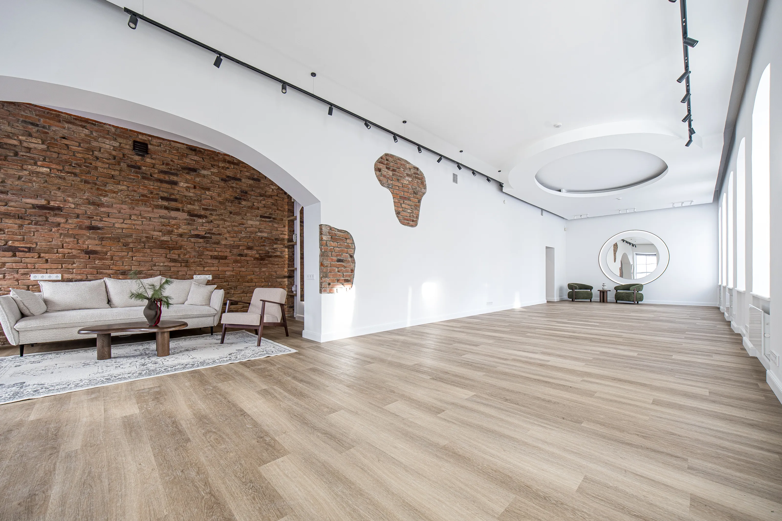 Erdvi studijos salė su arka, poilsio zona, plytų siena už jos ir apvaliu lubų elementu