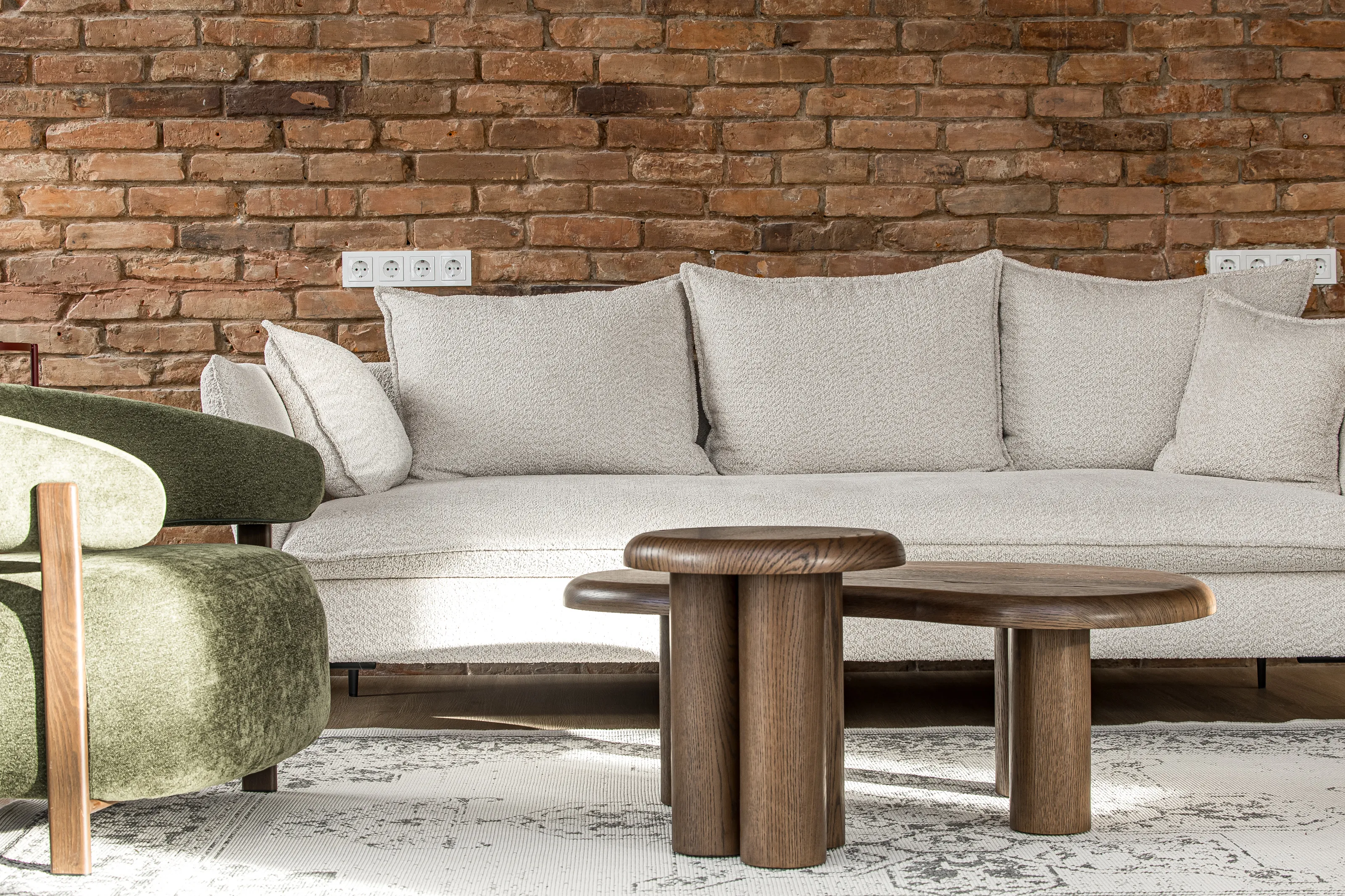 Žalias fotelis ir kreminės spalvos sofa su mediniu staliuku prie plytų sienos